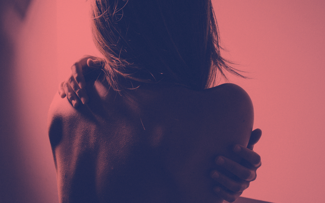Woman facing away from camera with arms wrapped around herself