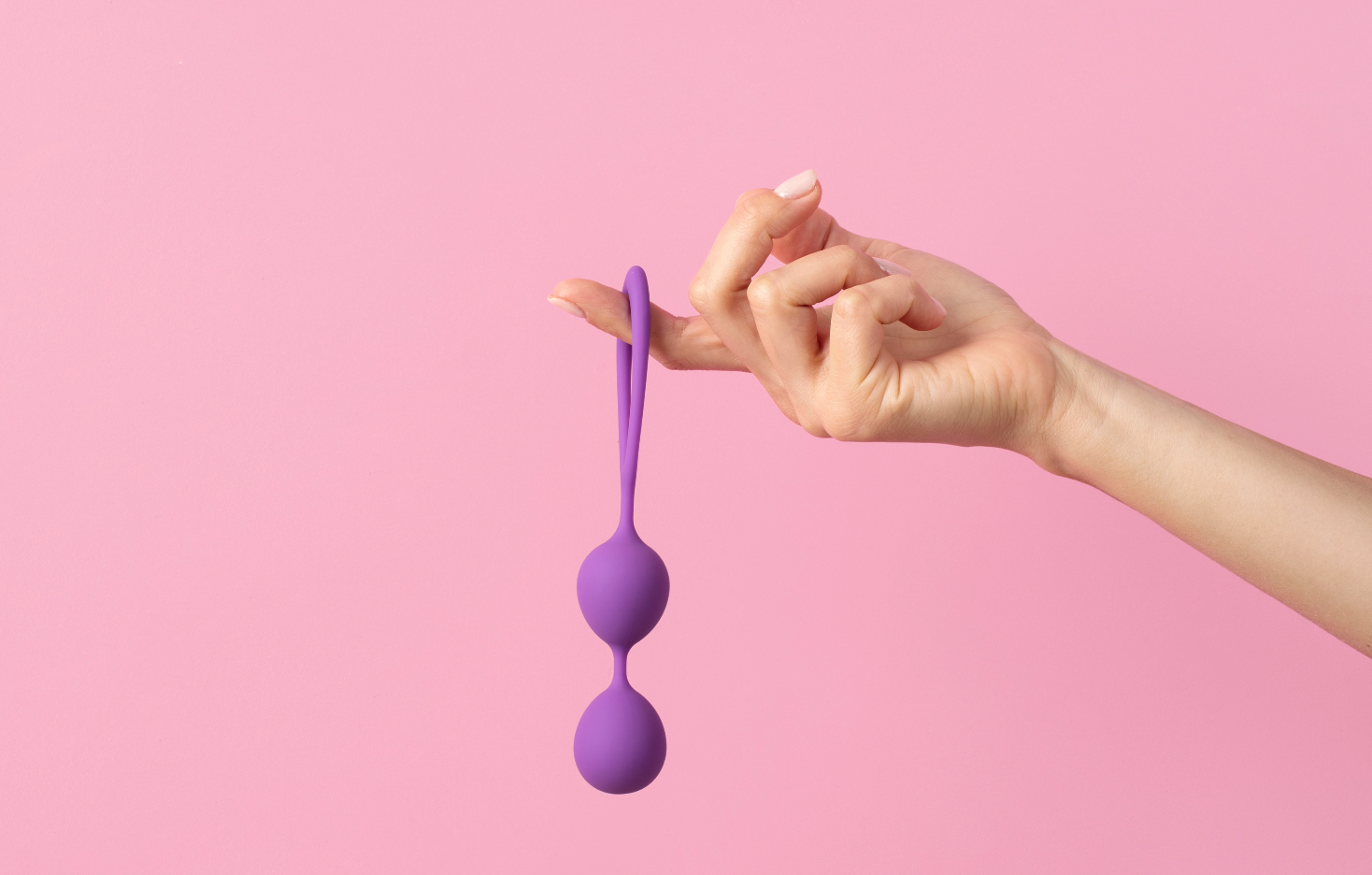 woman's hand holding Kegel balls on a pink background